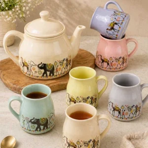 Colorful ceramic tea set with folk art elephant design including teapot and pastel mugs placed in an aesthetic kitchen setup