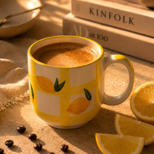 Handmade ceramic coffee mug with hand-painted lemon design by Cerami29 placed on a cozy coffee table.